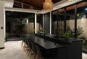 A modern kitchen with a black marble countertop, wooden chairs, a sink, and potted plants. - 400 m from Playa Negra, 3 bedrooms with air conditioning, swimming pool (Puerto Viejo de Talamanca)