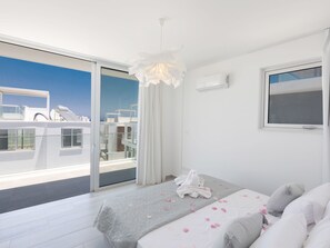Una camera da letto moderna con un balcone, un letto con petali di rosa e vista sul mare.