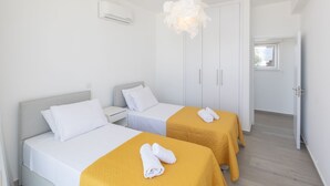 Ett hotellrum med två sängar, en vit luftkonditioneringsanläggning, en vit dörr och utsikt över omgivningarna genom ett fönster.