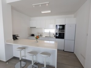 A modern kitchen with white cabinetry, a central island with bar stools, a built-in oven, and a refrigerator. - Protaras Olivine Villa OL9 by Interhome (Protaras)