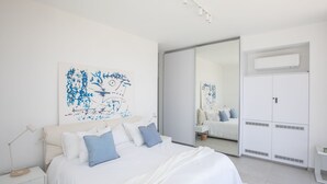 Moderni makuuhuone, jossa on suuri sänky, valkoiset seinät ja abstraktia taidetta.