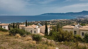 Un quartier résidentiel situé sur la côte, avec des maisons dotées de toits plats et de panneaux solaires, offrant une vue sur la mer et sur des montagnes lointaines.