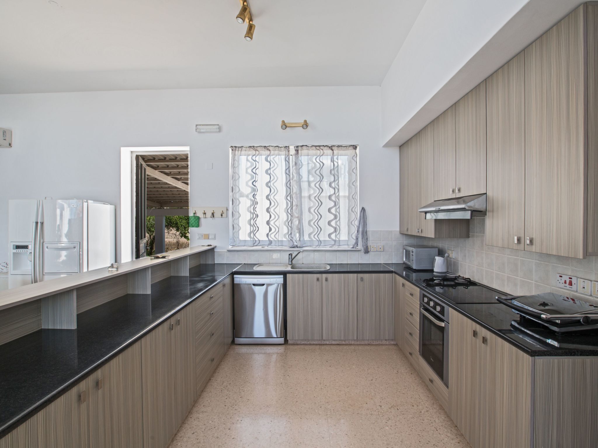 A modern kitchen with wooden cabinets, a stainless steel dishwasher, and a black countertop.