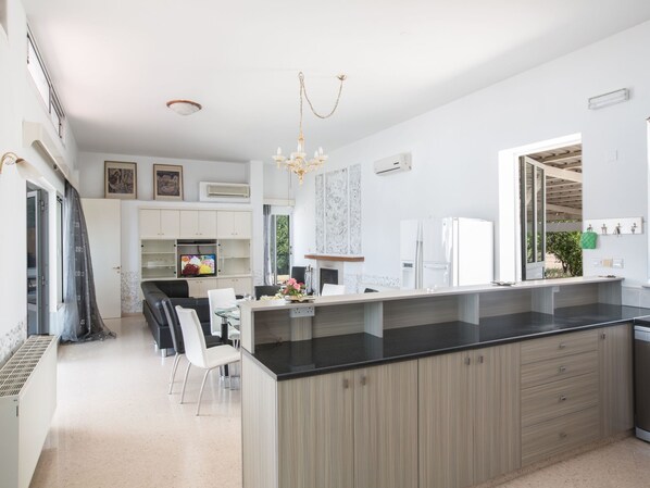 A modern kitchen with a large island, white cabinetry, and a dining area with chairs.
