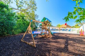 A playground with a swing set and a climbing structure, surrounded by trees and a pool area. - Luxury 5BR  Heated Pool, Pickleball & Hot Tub (Seminole)