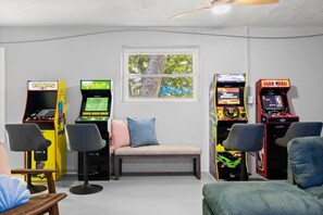 A room with arcade games, a bench, and a window with a tree view. - Luxury 5BR  Heated Pool, Pickleball & Hot Tub (Seminole)