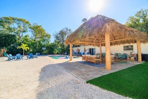 Una casa amb teulada de palla, piscina i mobiliari d'exterior.