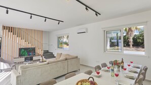 Una sala de estar moderna con sofá, televisión, mesa de comedor con sillas y una escalera.