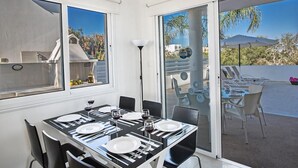Un coin repas avec une table dressée pour quatre personnes, de grandes fenêtres et une vue sur l’extérieur.