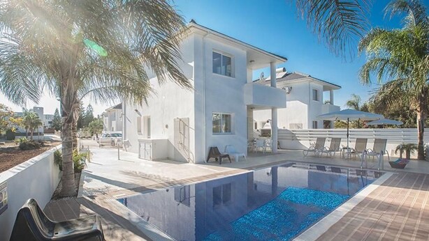 Une maison moderne avec une piscine, entourée de palmiers et sous un ciel dégagé.
