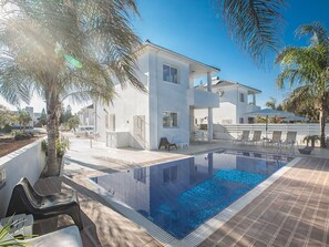 Ett modernt hus med en swimmingpool, omgivet av palmer och en klar himmel.