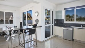 Une cuisine moderne avec un coin repas, de grandes fenêtres et une vue sur l’extérieur.
