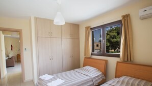 Un dormitorio con dos camas individuales, un armario, una ventana con cortinas y un equipo de aire acondicionado.