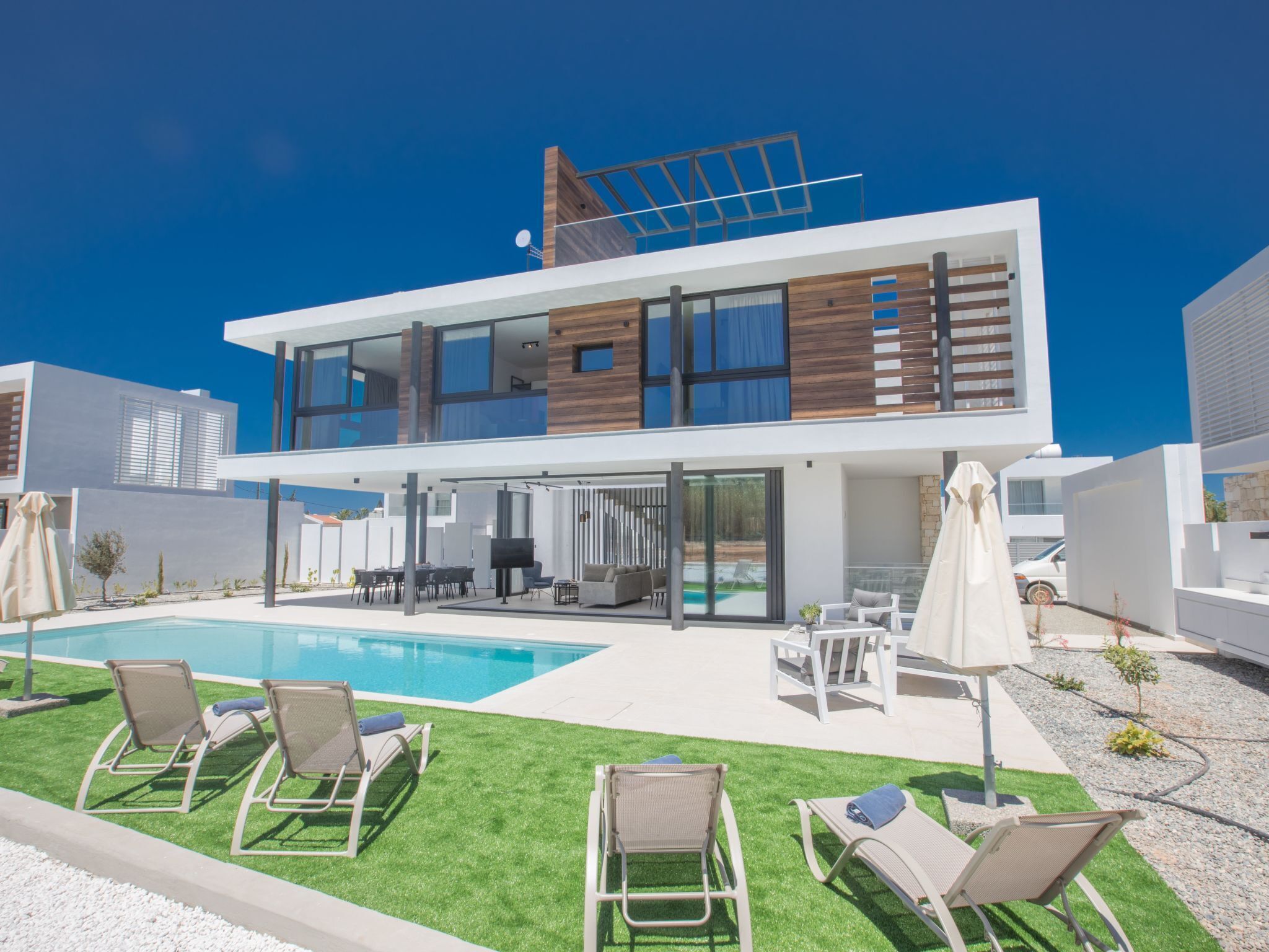 Ein modernes, zweistöckiges Haus mit Swimmingpool, Außenmöbeln und einer Terrassenanlage.