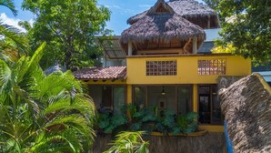 A yellow building with a thatched roof, surrounded by lush greenery. - Amare Las Villas (Sayulita)