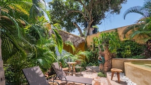 A patio with lounge chairs, a small table, and a water feature surrounded by lush greenery and a thatched-roof structure. - Amare Las Villas (Sayulita)