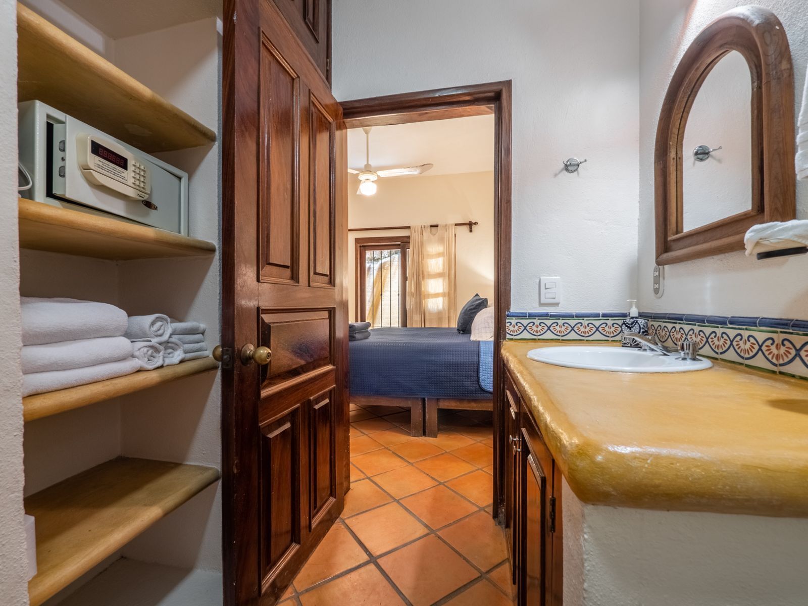 A bathroom with a wooden door, a shelf with towels, a sink with a decorative tile backsplash, and a mirror.