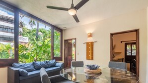 A modern dining area with a glass table, grey upholstered chairs, and a dark ceiling fan. - Amare Las Villas (Sayulita)
