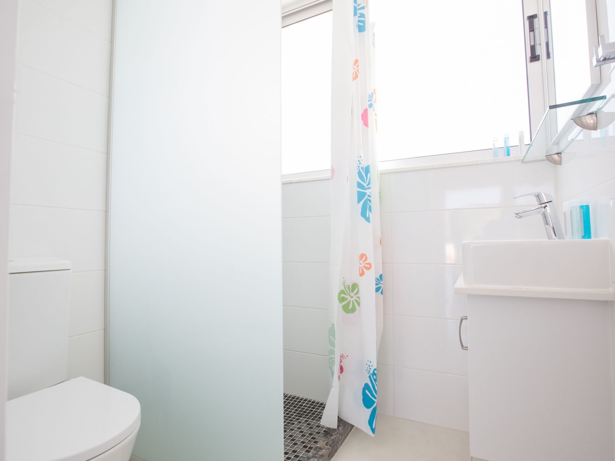 Ein Badezimmer mit Toilette, einer Dusche mit Blumenmuster am Vorhang und einem Waschbecken mit Spiegel darüber.