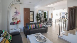 Una sala de estar moderna con un sofá, una mesa de centro y una lámpara de pie. Se ve una escalera que sube a otro nivel.