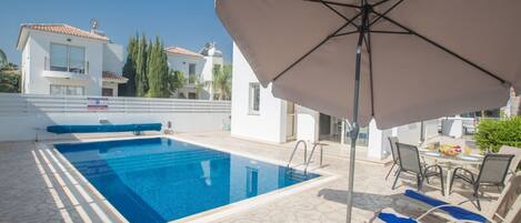 A swimming pool with lounge chairs and umbrellas, surrounded by buildings.