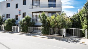 A two-story building with a balcony on the upper floor, surrounded by greenery and a white fence. - Komfortable Wohnung mit Balkon by Interhome (Ayia Napa)
