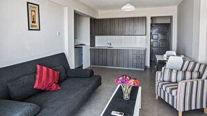 A modern living room with a grey sofa, a striped sofa, a coffee table with a vase of flowers, and a kitchen in the background. - Komfortable Wohnung mit Balkon by Interhome (Ayia Napa)