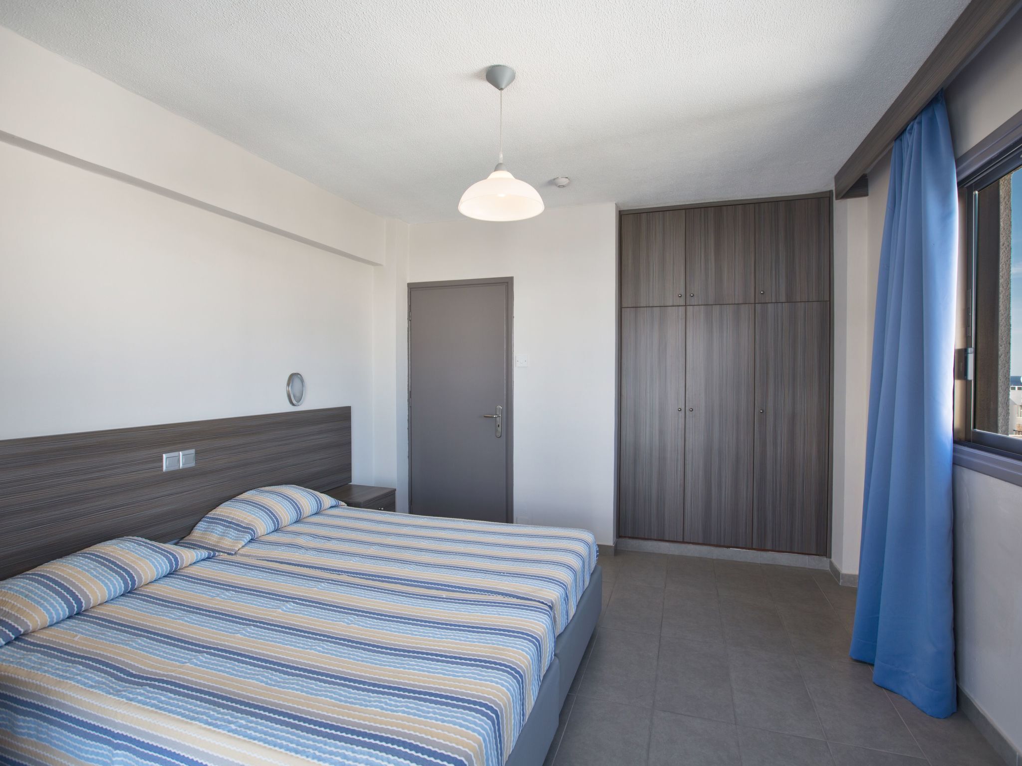 Una camera d'albergo moderna con un letto, un armadio e una finestra con tende.