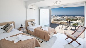Moderni hotellihuone, jossa on kaksi sänkyä, parveke, jolta on näkymä kaupunkiin ja merelle, sekä aurinkotuoli.