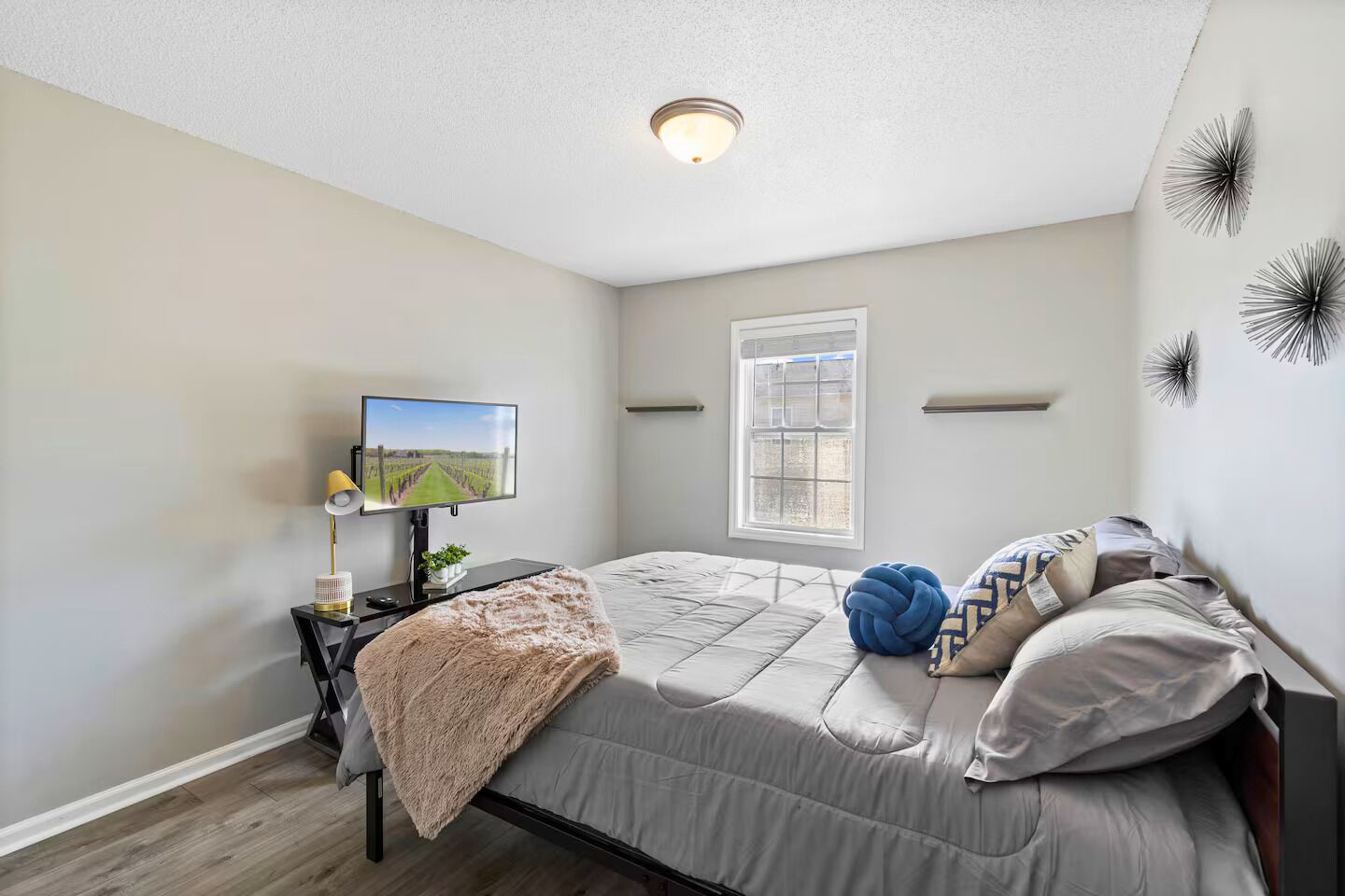 A bedroom with a bed, a TV, a desk with a lamp, a window, and wall decorations.