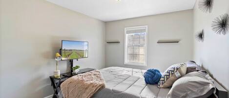 A bedroom with a bed, a TV, a desk with a lamp, a window, and wall decorations.