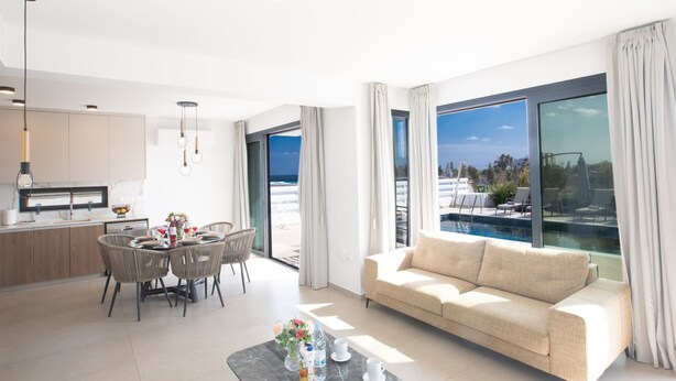 A modern living room with a sofa, dining area, and a view of the sea.
