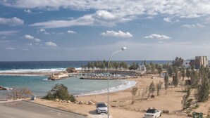 A coastal view with a beach, parked cars, and a clear sky.
