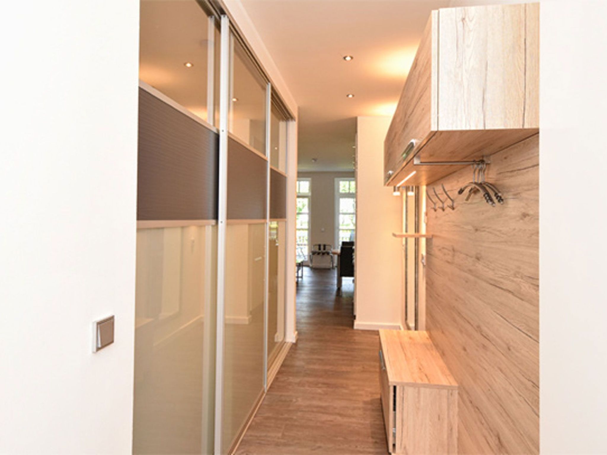 Un couloir doté d’une porte coulissante en verre, d’un plancher en bois et d’un banc.