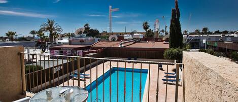 A rooftop pool with a glass table and chairs, surrounded by a metal railing.