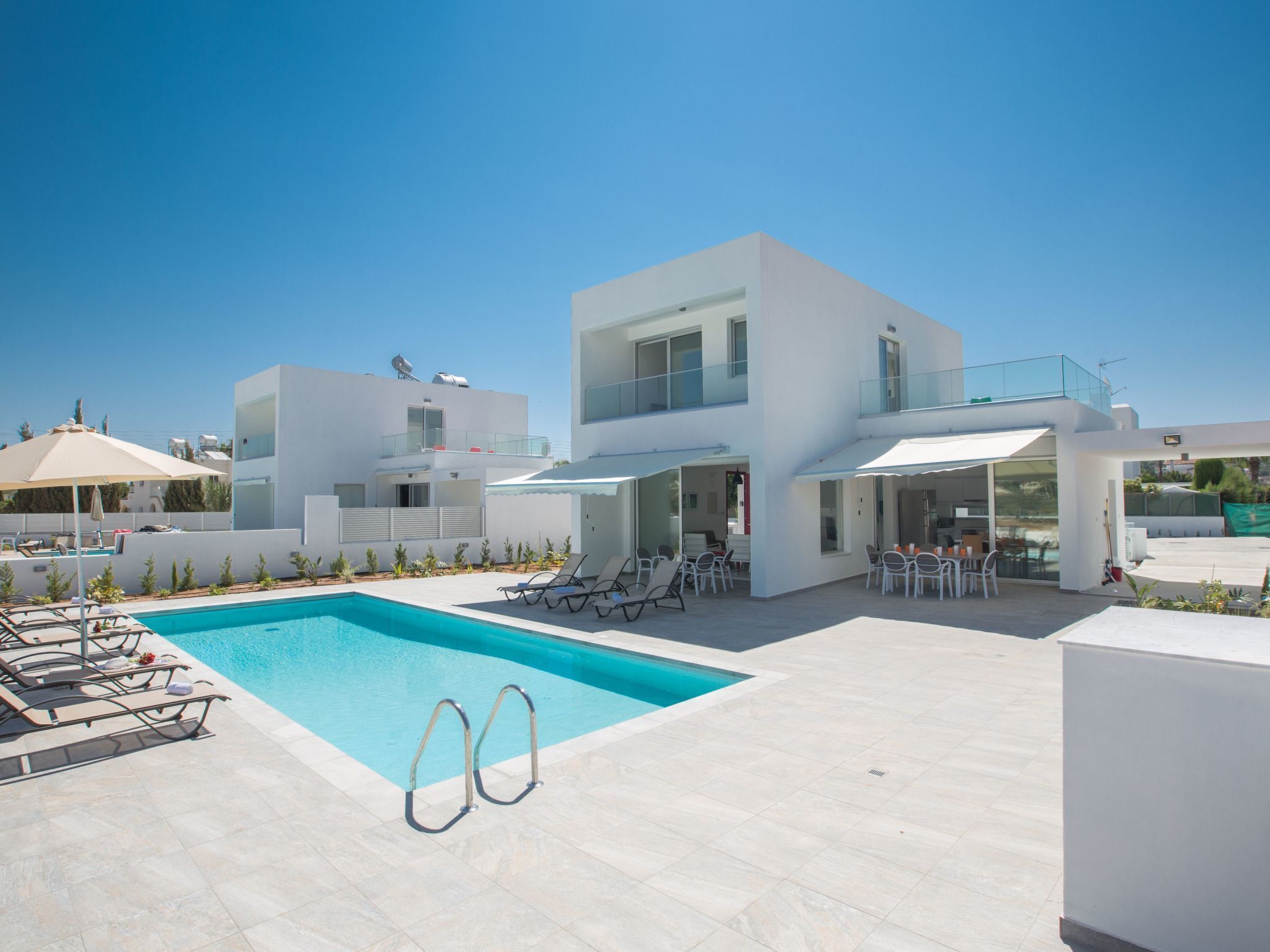 A modern poolside area with a clear blue pool, sun loungers, and a white building with large windows and a balcony.