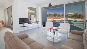 Una sala moderna con televisor, sofá y vista a la piscina.