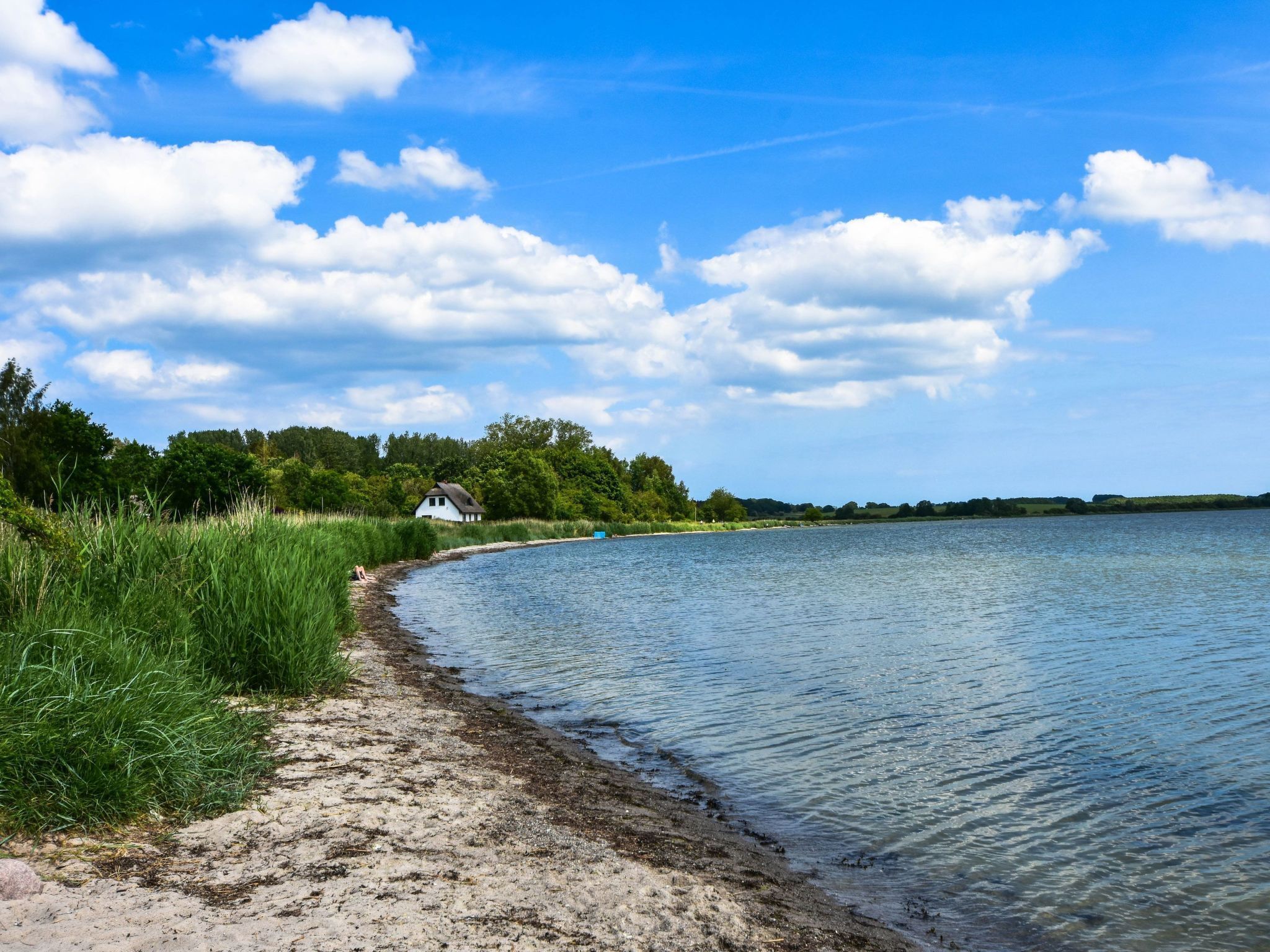 A lakeside view with a sandy path leading to a house by the water.