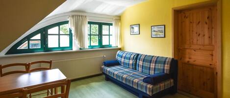 Una habitación con una mesa de comedor, sillas, un sofá, una ventana con cortinas y una puerta.