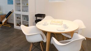 A dining area with a round table, white chairs, a white cabinet with glassware, and a hanging light fixture. - Appartement Sieben in Ostseebad Binz by Interhome (Binz)