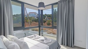 A modern bedroom with a large window, a bed with white linens, and a view of a residential area. - Protaras Elite Perle Villa EP3C by Interhome (Protaras)