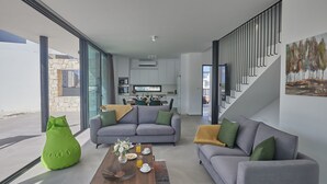 A modern living room with two grey sofas, a green bean bag, and a coffee table with drinks and flowers. A staircase with a railing is visible in the background. - Protaras Elite Perle Villa EP3C by Interhome (Protaras)