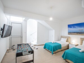 A hotel room with a foosball table, two beds with teal bedding, a TV mounted on the wall, and a painting of a beach scene. - Schöne, topmoderne Ferienvilla auf Zypern by Interhome (Paralimni)