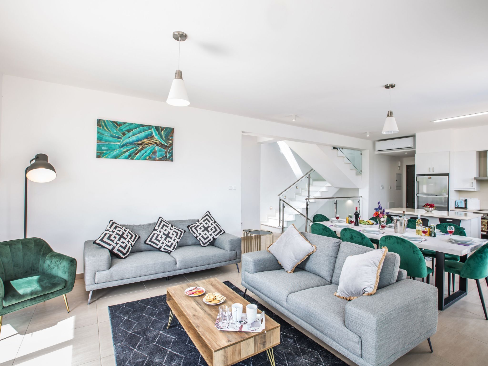 A modern living room with a grey sofa, a wooden coffee table, and a dining area with green chairs.