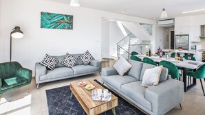 A modern living room with a grey sofa, a wooden coffee table, and a dining area with green chairs. - Schöne, topmoderne Ferienvilla auf Zypern by Interhome (Paralimni)