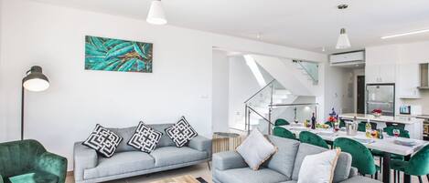 A modern living room with a grey sofa, a wooden coffee table, and a dining area with green chairs.