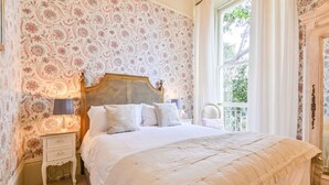 Ein Schlafzimmer mit floraler Wandgestaltung, einem hölzernen Kopfende, einer weißen Bettdecke und einem Nachttisch mit Lampe.