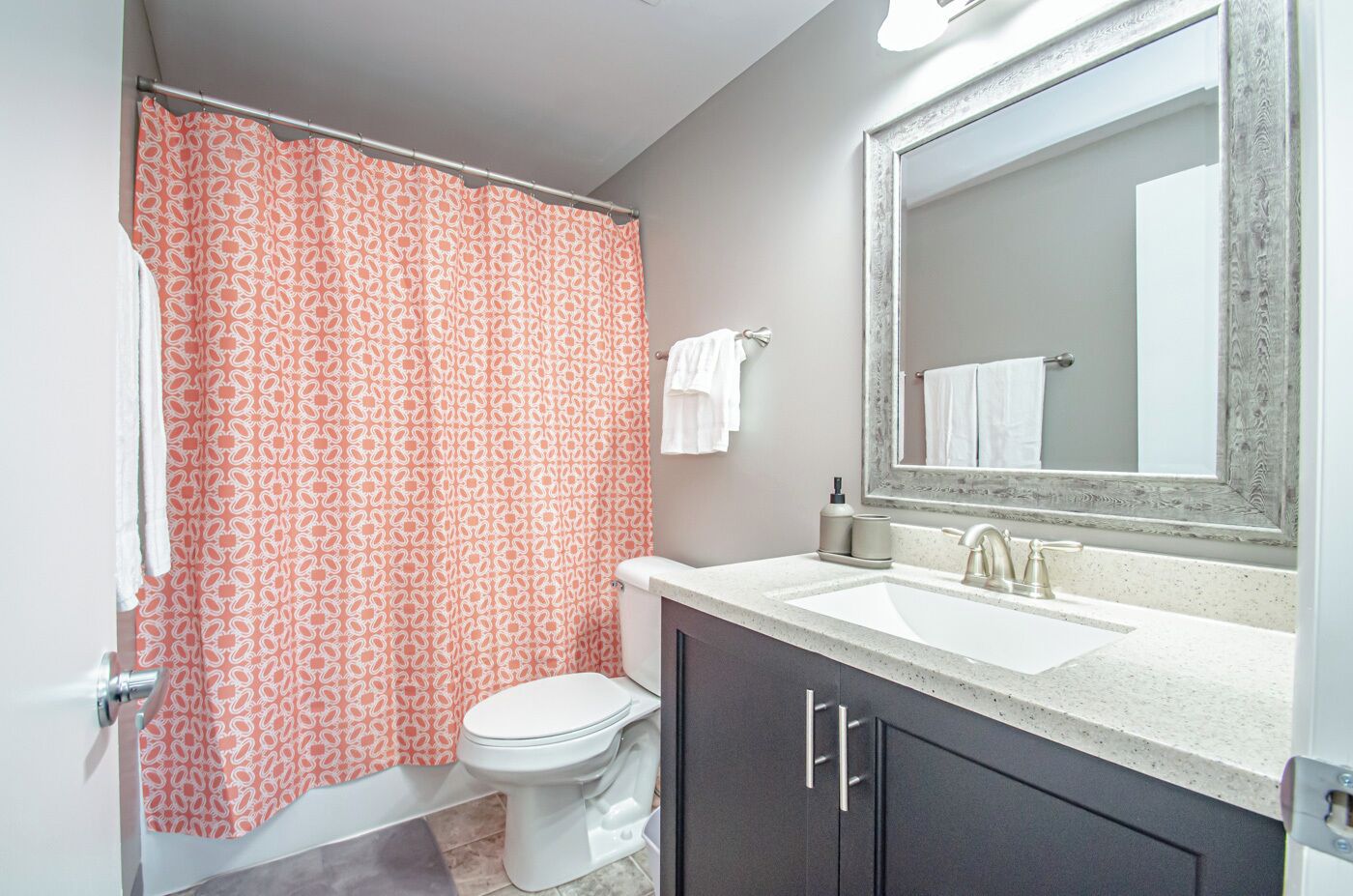 A bathroom with a patterned shower curtain, a toilet, a sink with a mirror, and dark cabinets.