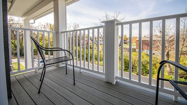 A covered porch with a white railing, a metal bench, and a view of a residential neighborhood.