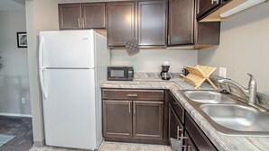 A compact kitchen with dark brown cabinets, a white refrigerator, a microwave, a coffee maker, and a sink with a modern faucet.